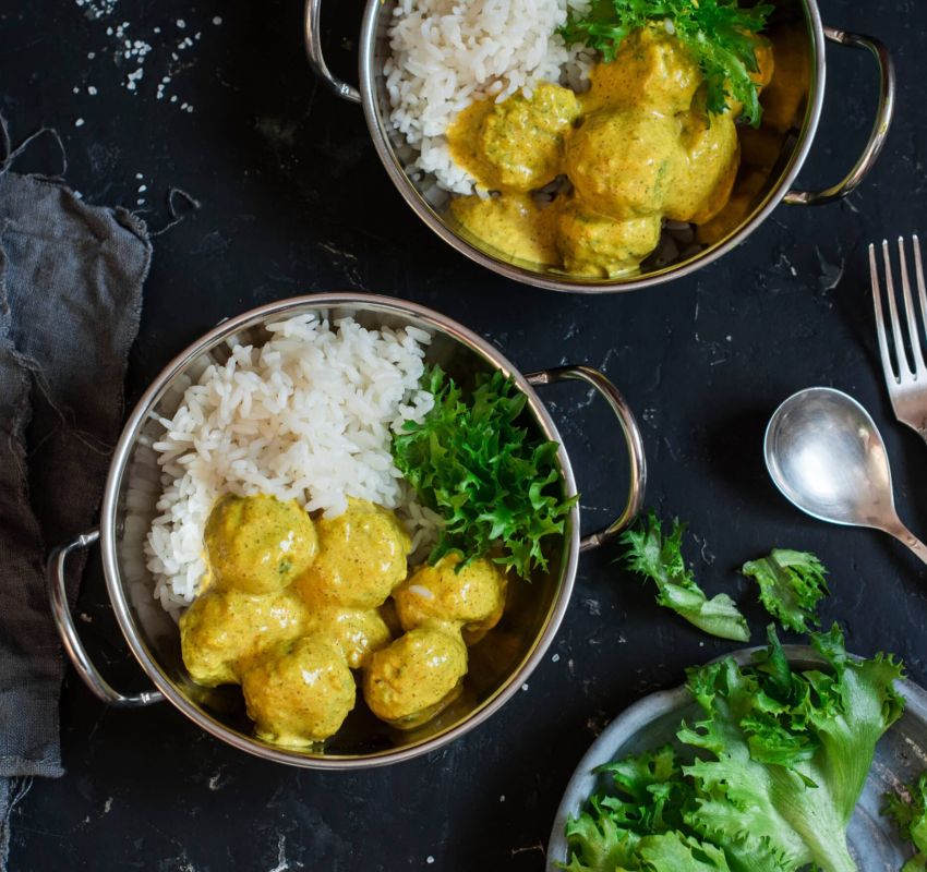 Zwei Schüsseln Hühnercurry mit Reis auf einem Tisch.