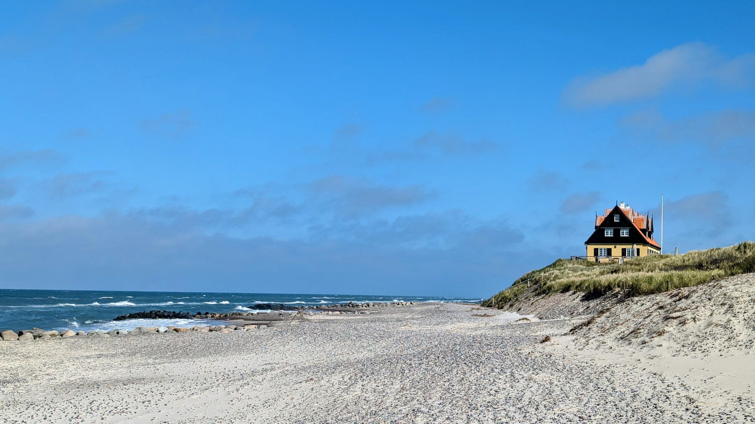 Ein kleines Haus liegt oben an einem Sandstrand.