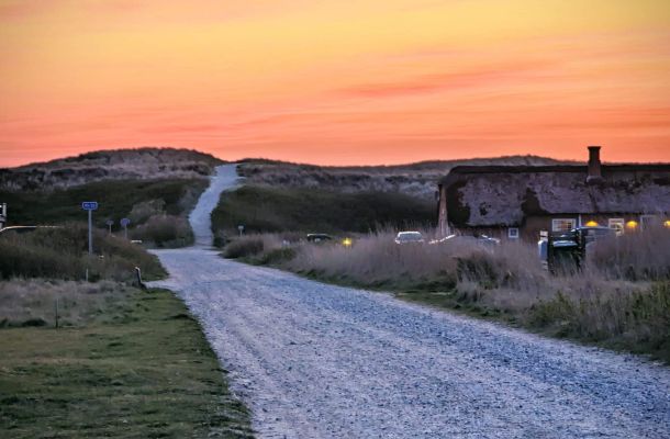 Eine unbefestigte Straße, die bei Sonnenuntergang zu einem Haus führt.