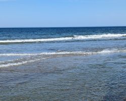 Ein Strand mit Wellen und Sand an einem sonnigen Tag.
