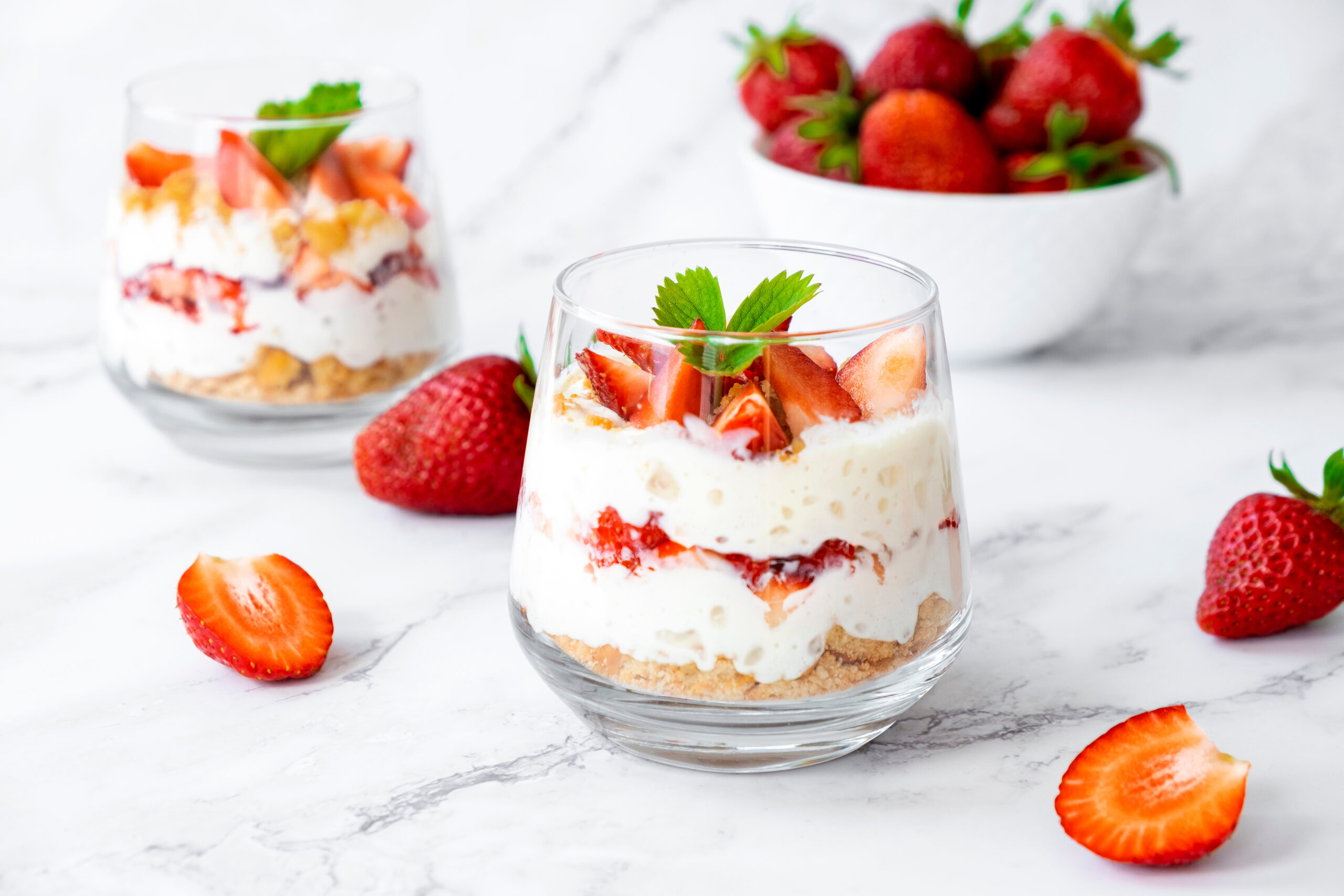 Zwei Glasdesserts mit Erdbeeren und Schlagsahne.